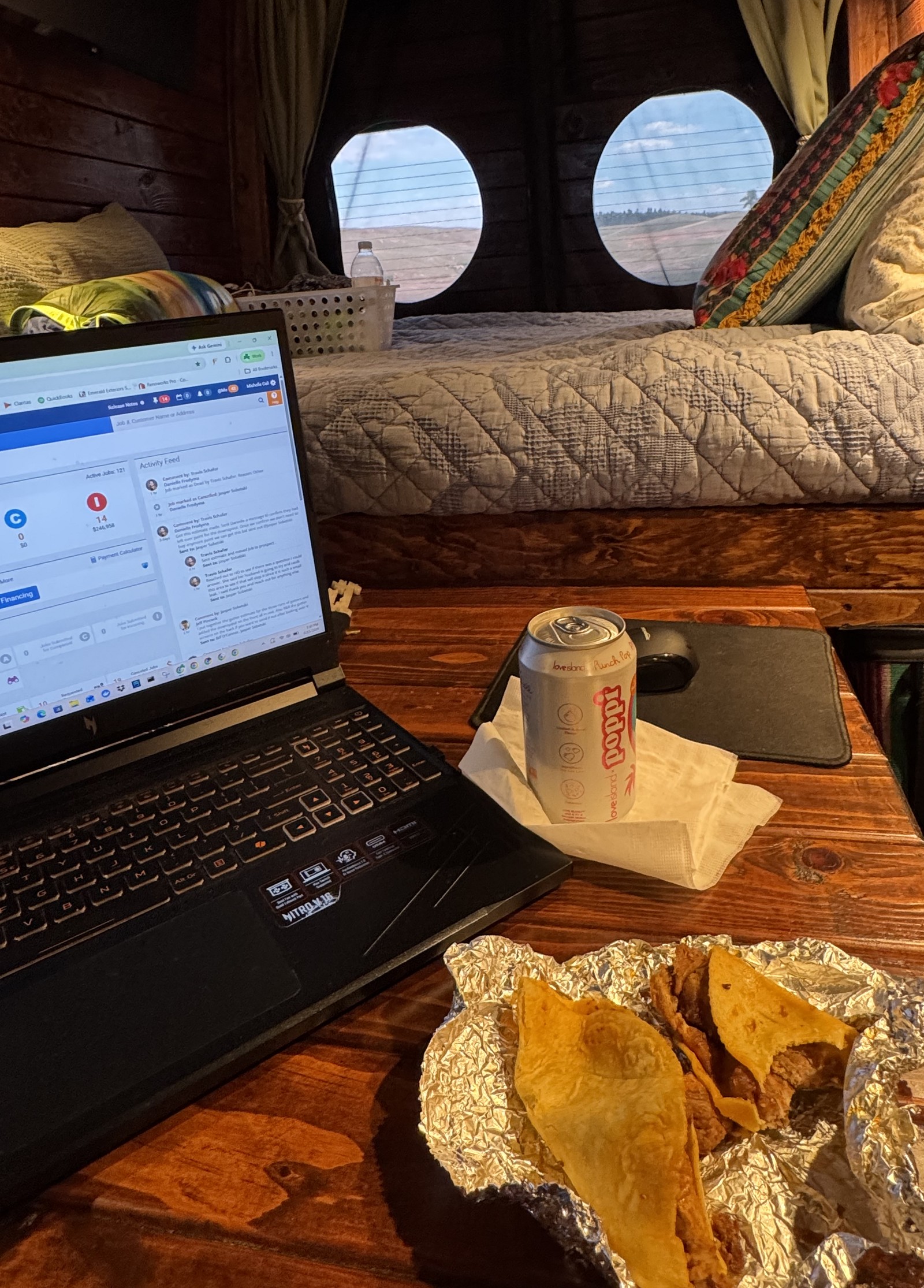 A laptop open on the table of a Sprinter van, with lunch beside it and prairie through the round windows.